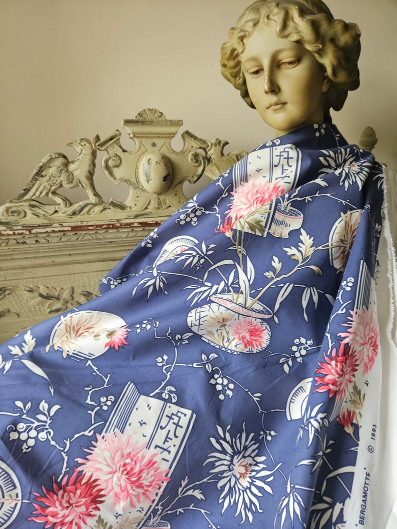 May include: A piece of blue fabric with a floral pattern featuring pink and white flowers, bamboo, and Japanese characters. The fabric is draped over a statue's shoulders. The fabric has a white edge with text.
