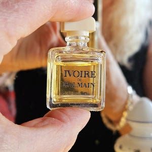 May include: A small, clear glass bottle of perfume with a white cap. The bottle is labeled "Ivoire de Balmain".