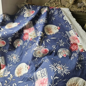 May include: A navy blue fabric with a floral pattern featuring pink chrysanthemums, white fans, and stylized vases. The design includes bamboo stalks and script-like elements, creating an Asian-inspired aesthetic. The fabric is draped, showcasing its texture and design.