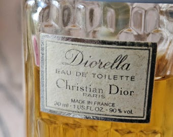 May include: A clear glass bottle with a gold liquid inside. The label reads "Diorella Eau de Toilette Christian Dior Paris Made in France 30 ml - 1 US.FL.OZ. - 90% vol."