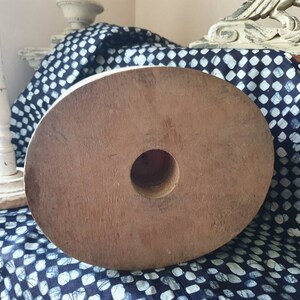 May include: A large, round, wooden spool with a hole in the center. The spool is brown and has a natural wood finish. It is sitting on a blue and white patterned fabric.
