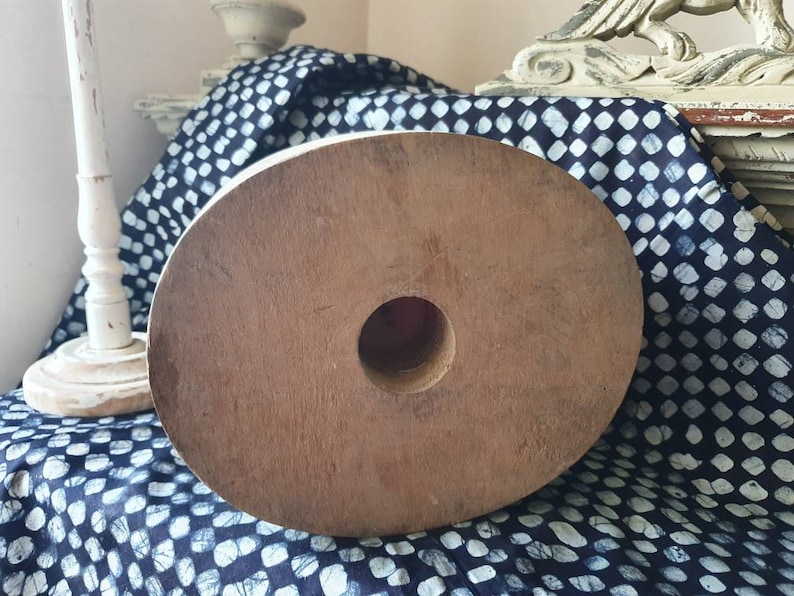 May include: A large, round, wooden spool with a hole in the center. The spool is brown and has a natural wood finish. It is sitting on a blue and white patterned fabric.