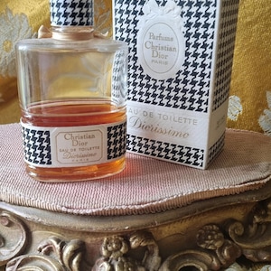 May include: A vintage bottle of Diorissimo Eau de Toilette perfume by Christian Dior. The bottle is clear glass with a black and white houndstooth pattern on the label. The box is also black and white houndstooth with the words "Parfums Christian Dior Paris" and "Eau de Toilette Diorissimo" printed on it.