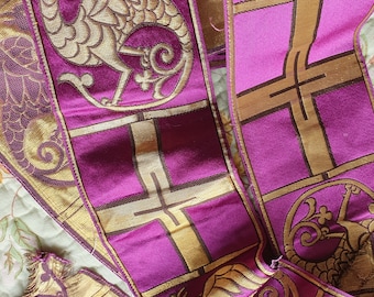 May include: A purple and gold fabric ribbon with a repeating pattern of a dragon, a cross, and a floral design. The ribbon is woven with a textured, raised design.