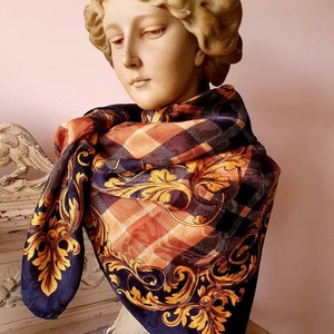 Puede incluir: Una bufanda de seda negra con un patrón de cuadros dorados y naranjas y diseños florales dorados. La bufanda está drapeada alrededor de un busto de yeso.