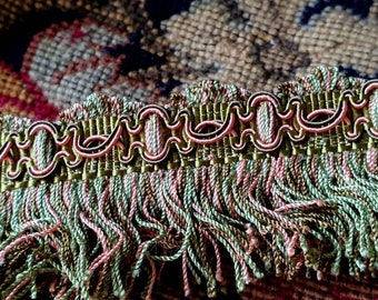 May include: Green and pink fringe trim with a decorative woven design. The trim has a scalloped edge and a fringe that is about 2.5 cm long.