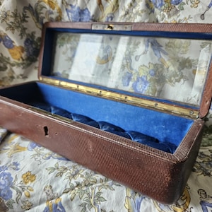 May include: A vintage wooden box with a glass top and blue velvet lining. The box has a keyhole and is lined with a blue velvet interior.