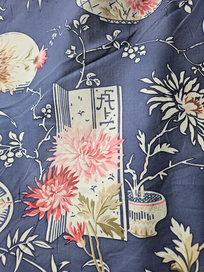 May include: Close-up of a navy blue fabric with a floral pattern. The design features large pink and white chrysanthemums, stylized branches, and a decorative vase. A section of the fabric includes Japanese characters.
