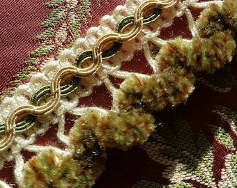May include: Close-up of a white and gold trim with green velvet tassels. The trim is made of a delicate crocheted fabric with a repeating pattern of loops and knots.