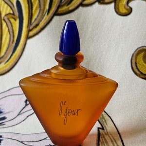 以下が含まれることがあります： 青いキャップが付いた茶色のガラス製の香水瓶。瓶はダイヤモンド型で、「Le Jour」という文字が書かれている。