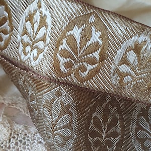May include: Close-up of a brown and white woven ribbon with a repeating floral pattern. The ribbon has a brown edge.