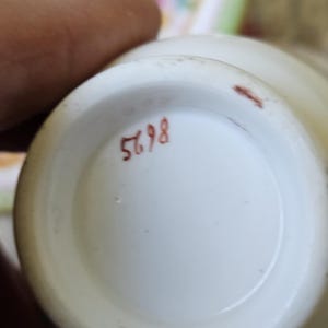 Op de afbeelding: De onderkant van een wit keramieken vat met het handgeschilderde rode nummer 5698. De basis is cirkelvormig met een gladde, geglazuurde afwerking en een kleine rode markering nabij de buitenrand, wat een duidelijk zicht geeft op de onderkant.