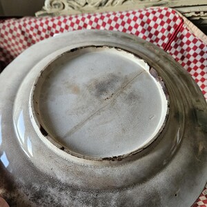 May include: The underside of a white ceramic plate with a crack running down the center. The plate has a brown rim and a rough, textured surface.