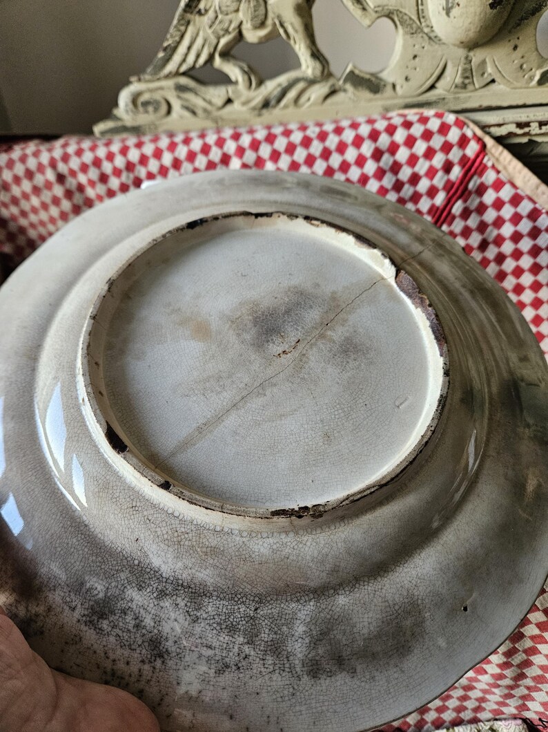 May include: The underside of a white ceramic plate with a crack running down the center. The plate has a brown rim and a rough, textured surface.