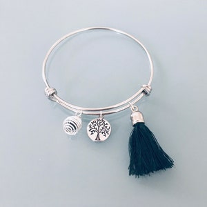 May include: Silver bangle bracelet with a black tassel charm, a tree of life charm, and a silver wire ball charm.