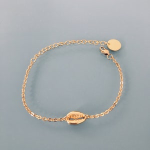 May include: A gold chain bracelet with a seashell charm and a small gold disc charm. The bracelet has a lobster clasp closure.