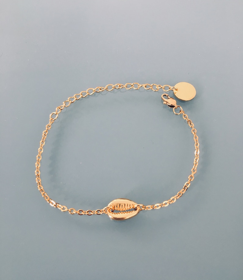 May include: A gold chain bracelet with a seashell charm and a small gold disc charm. The bracelet has a lobster clasp closure.