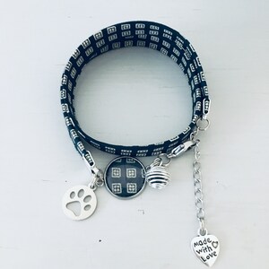 Peut inclure: Un bracelet en tissu à motif noir et blanc avec des breloques argentées, dont une empreinte de patte, un breloque rond avec le même motif que le bracelet, une petite boule argentée et un breloque en forme de cœur avec le texte "Made with Love".