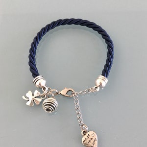 May include: A navy blue braided bracelet with silver beads and charms. The charms include a four-leaf clover, a round ball, and a heart with the text "made with love".