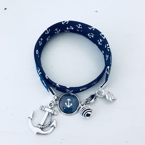 Könnte beinhalten: Ein marineblaues Armband mit einem weißen Ankermuster. Das Armband hat einen silbernen Anker-Anhänger, einen silbernen Anhänger mit einem Wirbelmuster und einen silbernen Anhänger mit dem Wort "Liebe" darauf.