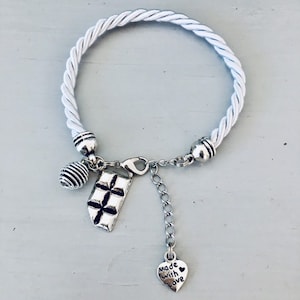 Peut inclure: Bracelet en corde blanche avec des breloques argentées. Les breloques comprennent un cœur avec le texte "made with love", un breloque carré avec un motif en grille et un breloque en spirale.