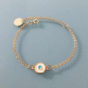 Peut inclure: Un bracelet en chaîne dorée avec un petit charme rond représentant un œil maléfique bleu et blanc.