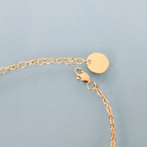 May include: A gold chain bracelet with a round, gold charm. The chain is made of small, linked circles.