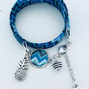 Könnte beinhalten: Ein blaues und schwarzes Armband aus Stoff mit Chevron-Muster, einem silbernen Verschluss, einem Ananas-Anhänger, einem runden Anhänger mit Chevron-Muster, einem silbernen Käfig-Anhänger und einem Herz-Anhänger mit der Aufschrift "Made with Love".