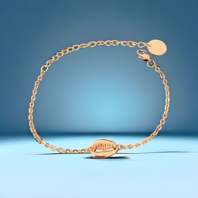 May include: A gold chain bracelet with a seashell charm. The bracelet has a lobster clasp and a small round disc charm.