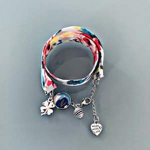 May include: A colourful fabric bracelet with a silver chain and charms. The charms include a four-leaf clover, a round charm with a floral pattern, a round metal ball, and a heart charm with the text "Made with Love".
