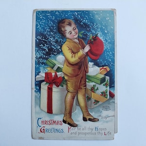 May include: Vintage Christmas postcard featuring a young person in a yellow suit holding a red sack. The background shows wrapped gifts and a snowy scene. The card has the words "Christmas Greetings" and a holiday message.
