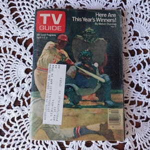 May include: A vintage TV Guide magazine featuring a baseball-themed cover with the text "Here Are This Year's Winners!" and "TV GUIDE" in a red box. The magazine has a price tag and is set on a white lace doily.