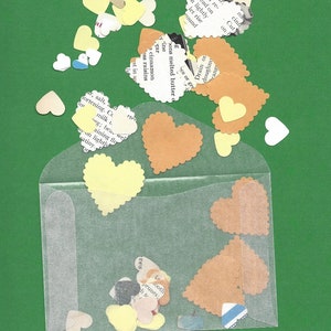 May include: A clear plastic envelope filled with colorful paper hearts. The hearts are in various shades of yellow, orange, and white. The envelope is on a green background.