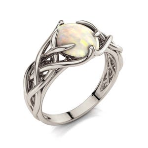 Puede incluir: Un anillo de plata con una piedra de ópalo blanco engastada en un diseño de nudo celta.