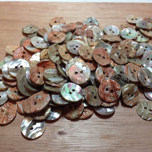 May include: A collection of assorted buttons with two holes each. The buttons have a mix of colors, including iridescent, brown, and tan. The buttons are made of a natural material, possibly shell, and have a glossy finish. Ideal for sewing and craft projects.