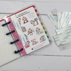 May include: A clear plastic binder with a pink and white glitter cover. The binder has a white page with a sloth sticker design. The text on the sticker reads "The heaters are in order at my store." and "NOPE,  Love is love, get your doors open." The sticker also includes a social media handle. The binder is open to reveal a blank white page. A clear plastic bag with adhesive strips is on the right side of the image.