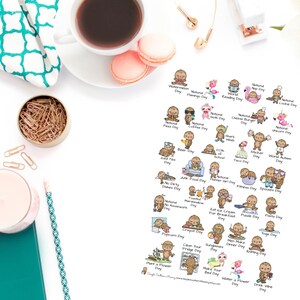 May include: A white paper sheet with various cartoon illustrations representing different days, such as National Pizza Day and World Reading Day. The sheet is surrounded by a cup of coffee, macarons, and stationery.