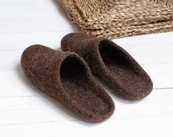 May include: A pair of brown wool slippers on a white wooden surface. The slippers are made of a soft, fuzzy material and have a simple, classic design.