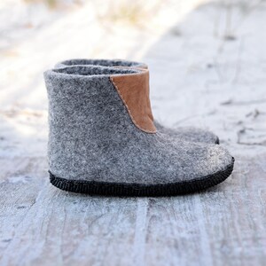 Puede incluir: Botas de fieltro gris con un detalle de cuero marr&oacute;n en la parte superior. Las botas tienen una suela negra y est&aacute;n dise&ntilde;adas para brindar calidez. Hechas de lana, son adecuadas para el clima fr&iacute;o. Miden aproximadamente 20 cm de alto.