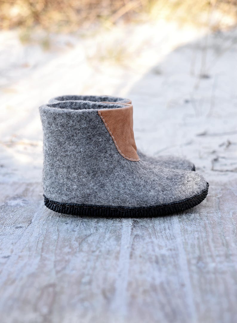 Puede incluir: Botas de fieltro gris con un detalle de cuero marr&oacute;n en la parte superior. Las botas tienen una suela negra y est&aacute;n dise&ntilde;adas para brindar calidez. Hechas de lana, son adecuadas para el clima fr&iacute;o. Miden aproximadamente 20 cm de alto.