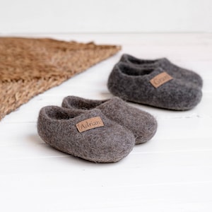 May include: Two pairs of grey wool slippers with personalised leather labels. One pair says "Adrian" and the other says "Grant".
