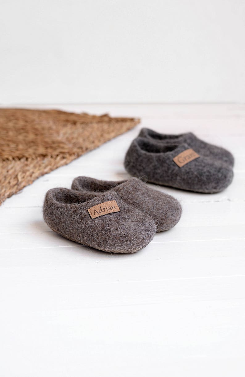 May include: Two pairs of grey wool slippers with personalised leather labels. One pair says "Adrian" and the other says "Grant".