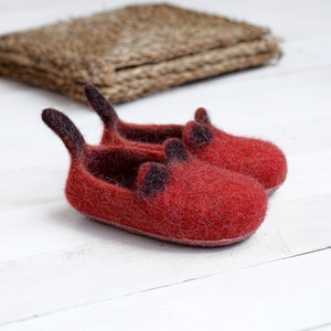 May include: A pair of red felt slippers with black felt accents. The slippers have a pointed toe and a small heel.
