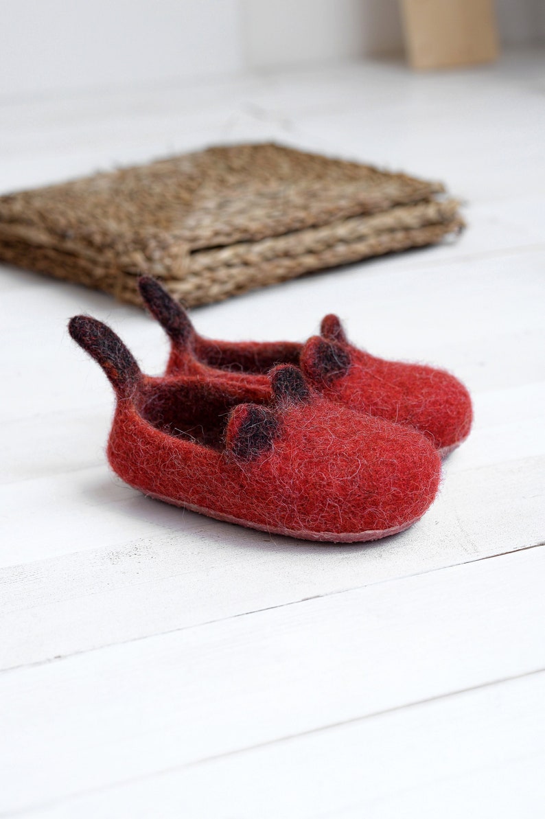 May include: A pair of red felt slippers with black felt accents. The slippers have a pointed toe and a small heel.