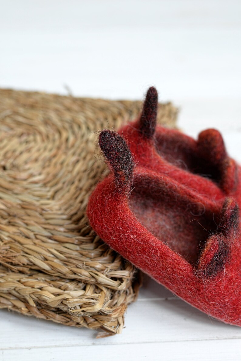 May include: Red felt slippers with black felt horns. The slippers are sitting on a woven straw mat.