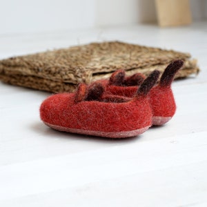 May include: A pair of red felt slippers with brown felt accents. The slippers have a pointed toe and a small heel.
