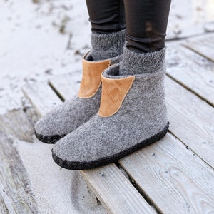 Puede incluir: Botas grises de lana afieltrada con un detalle de cuero marr&oacute;n. Las botas tienen una suela cosida negra y se muestran sobre una cubierta de madera. Las botas parecen c&aacute;lidas y c&oacute;modas, ideales para el clima fr&iacute;o. Miden unos 20 cm de alto.