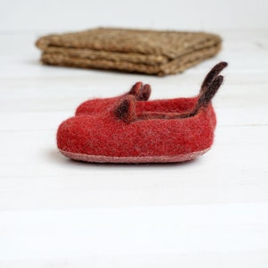 May include: A pair of red felt slippers with black felt accents. The slippers are on a white surface.