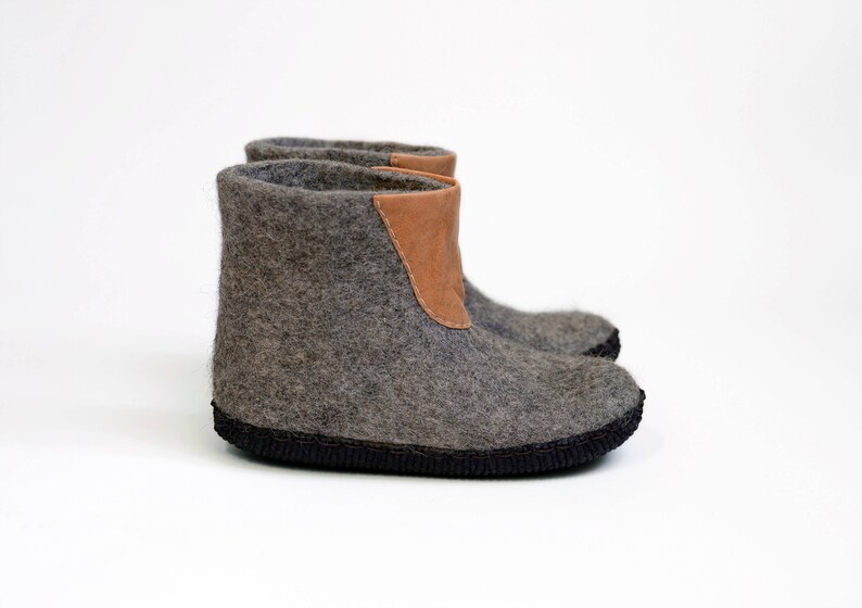 Puede incluir: Botas de fieltro gris con un detalle de cuero marr&oacute;n en el borde superior. Las botas tienen una suela negra y est&aacute;n dise&ntilde;adas para uso en interiores. El fieltro proporciona calidez y comodidad.