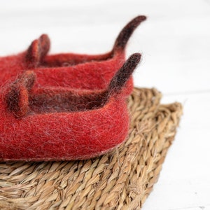 May include: Two red felt slippers with black felt accents. The slippers are sitting on a woven straw mat.